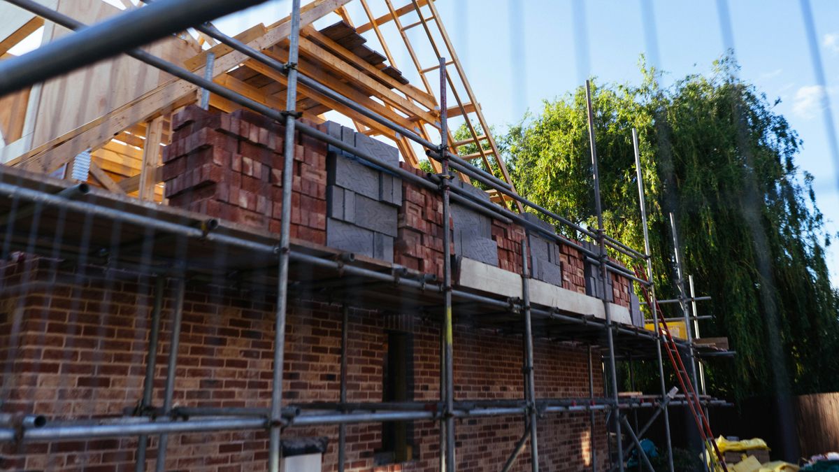 Een bakstenen woning in aanbouw met een stelling en een houten dakgebinte